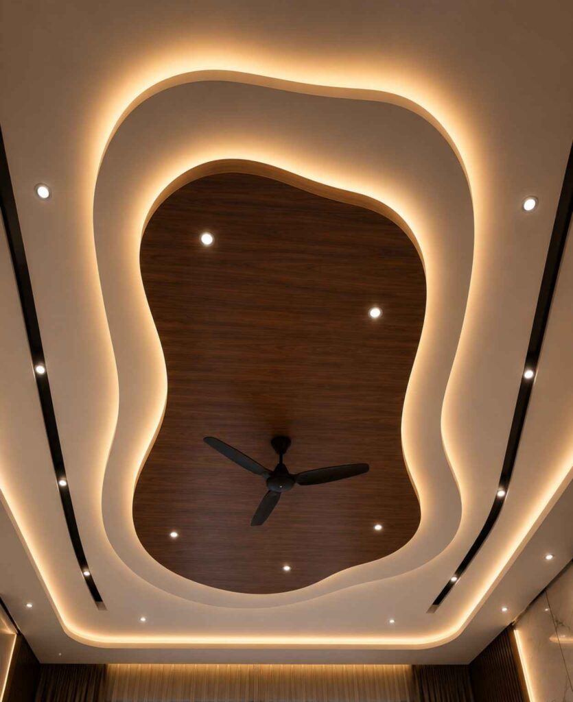 Modern organic false ceiling design with curved POP layers, wooden center panel, warm LED strip lighting, recessed spotlights, ceiling fan, and contemporary luxury interior styling.