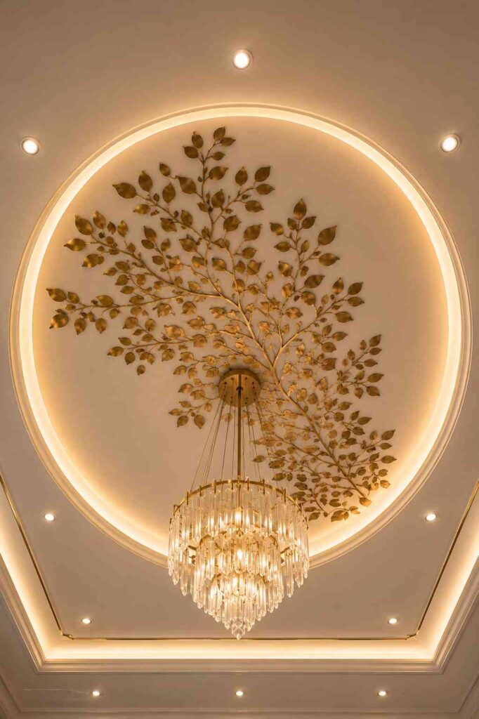 Luxury circular POP ceiling design with warm LED lighting, decorative golden tree artwork, crystal chandelier, recessed spotlights, and elegant false ceiling detailing in a modern interior.