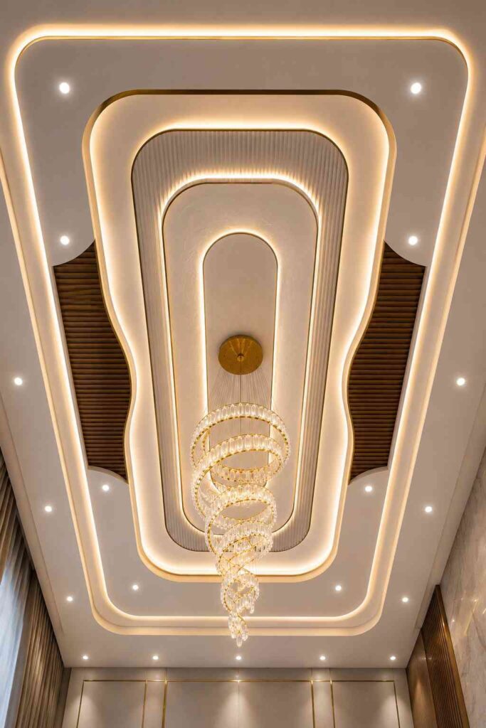 Luxury POP false ceiling featuring layered gypsum panels, recessed LED cove lighting, wooden ceiling accents, and a crystal spiral chandelier for an elegant living room interior.